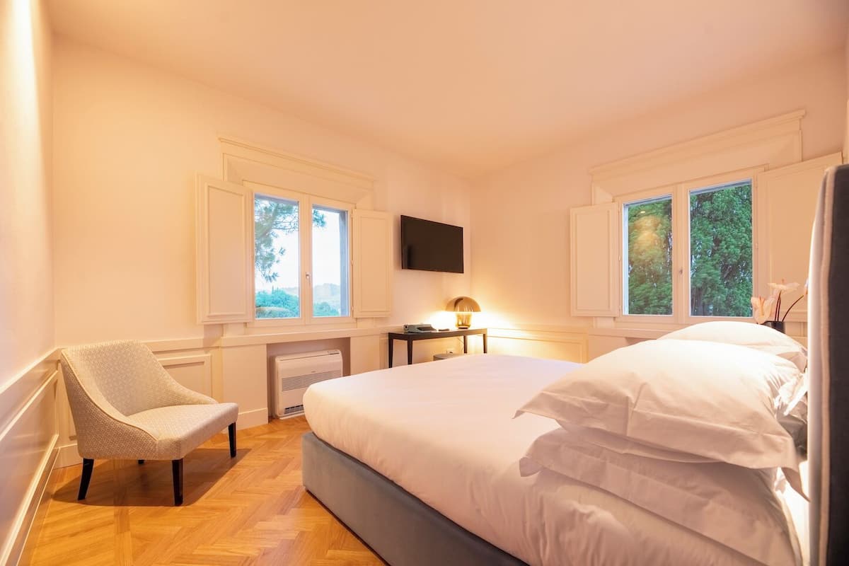 A bedroom with a large bed, a chair, a desk, and a TV.
