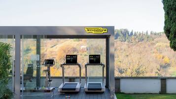 Un gimnasio moderno al aire libre con cintas de correr y una bicicleta estática, con vistas a un paisaje pintoresco.