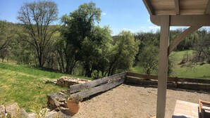 Un espace extérieur abrité doté d’une terrasse en bois, d’un mur en pierre et offrant une vue sur un paysage verdoyant parsemé d’arbres.