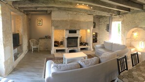 Un salon rustique avec des murs en pierres apparentes, une cheminée, un canapé blanc et un téléviseur.