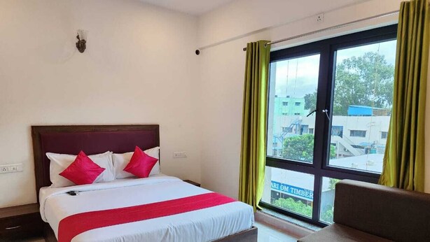 Una habitación de hotel con cama, sofá, ventana con cortinas y vistas a edificios.