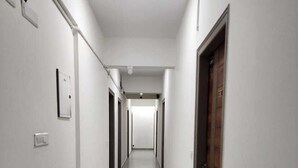 Un pasillo largo y estrecho con paredes blancas y suelo gris, que conduce a una puerta al final.