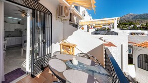A balcony with a table and chairs, a ceiling fan, and a view of the surrounding buildings and mountains. - Sunny 2 bed apartment in a complex with pools close to village centre and beach. (Nerja)