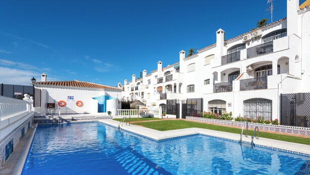 A swimming pool with a clear blue water surface, surrounded by white buildings with balconies and a tiled roof. - Sunny 2 bed apartment in a complex with pools close to village centre and beach. (Nerja)