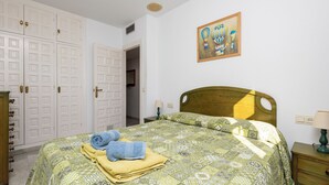 A bedroom with a bed, a nightstand, a lamp, a wardrobe, and a painting on the wall. - Sunny 2 bed apartment in a complex with pools close to village centre and beach. (Nerja)