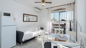 A compact living space with a white sofa, a glass table with chairs, a ceiling fan, and a view through a window with a metal gate. - Sunny 2 bed apartment in a complex with pools close to village centre and beach. (Nerja)