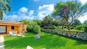 A sunny outdoor area with a stone wall, a small rock, and white lounge chairs. - Apartment in Porto Pollo Near Sea Beach (Palau)