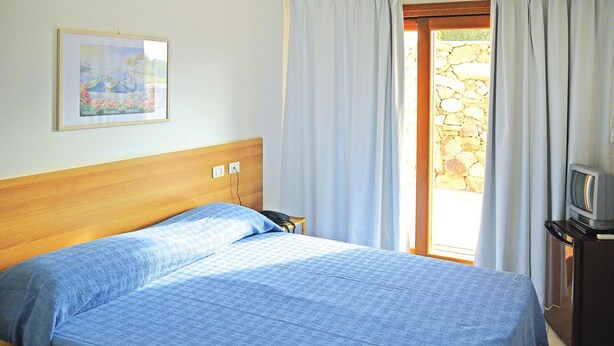 A bedroom with a bed, a painting on the wall, a television on a stand, and a stone wall outside the door. - Apartment in Porto Pollo Near Sea Beach (Palau)