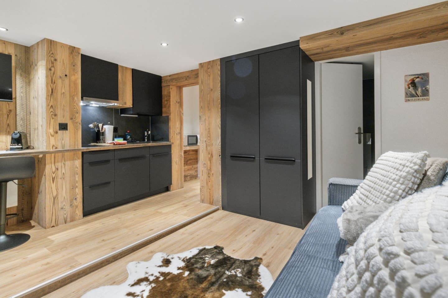 Une cuisine moderne agrémentée d’éléments en bois, un coin repas avec un tapis en peau de vache, et une chambre à coucher dotée d’un grand lit et d’un tableau représentant la Suisse.