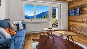 A room with a wooden interior, a sofa with a deer pillow, a cowhide rug, and a TV on the wall. - Charming studio near the ski slopes (Leukerbad)