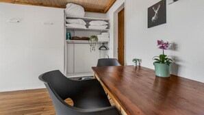 A room with a wooden ceiling, a wooden dining table, a black chair, a white shelf with folded towels, and a potted plant. - Charming studio near the ski slopes (Leukerbad)