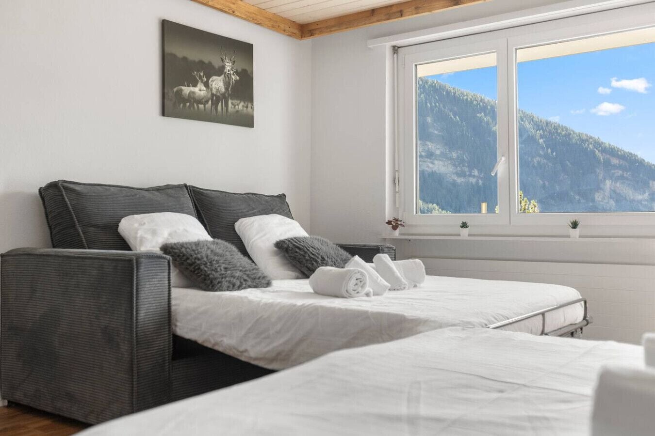 A bedroom with two beds, a large window with a mountain view, a painting of deer, and a wooden ceiling.
