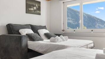 A bedroom with two beds, a large window with a mountain view, a painting of deer, and a wooden ceiling.