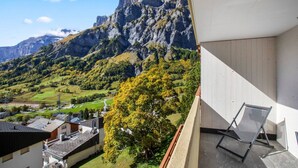 A balcony with a view of a mountainous landscape, a chair, and a building with a sloped roof. - Charming studio near the ski slopes (Leukerbad)