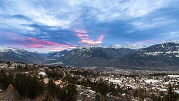 Paisaje montañoso con un pueblo en primer plano y picos nevados al fondo.