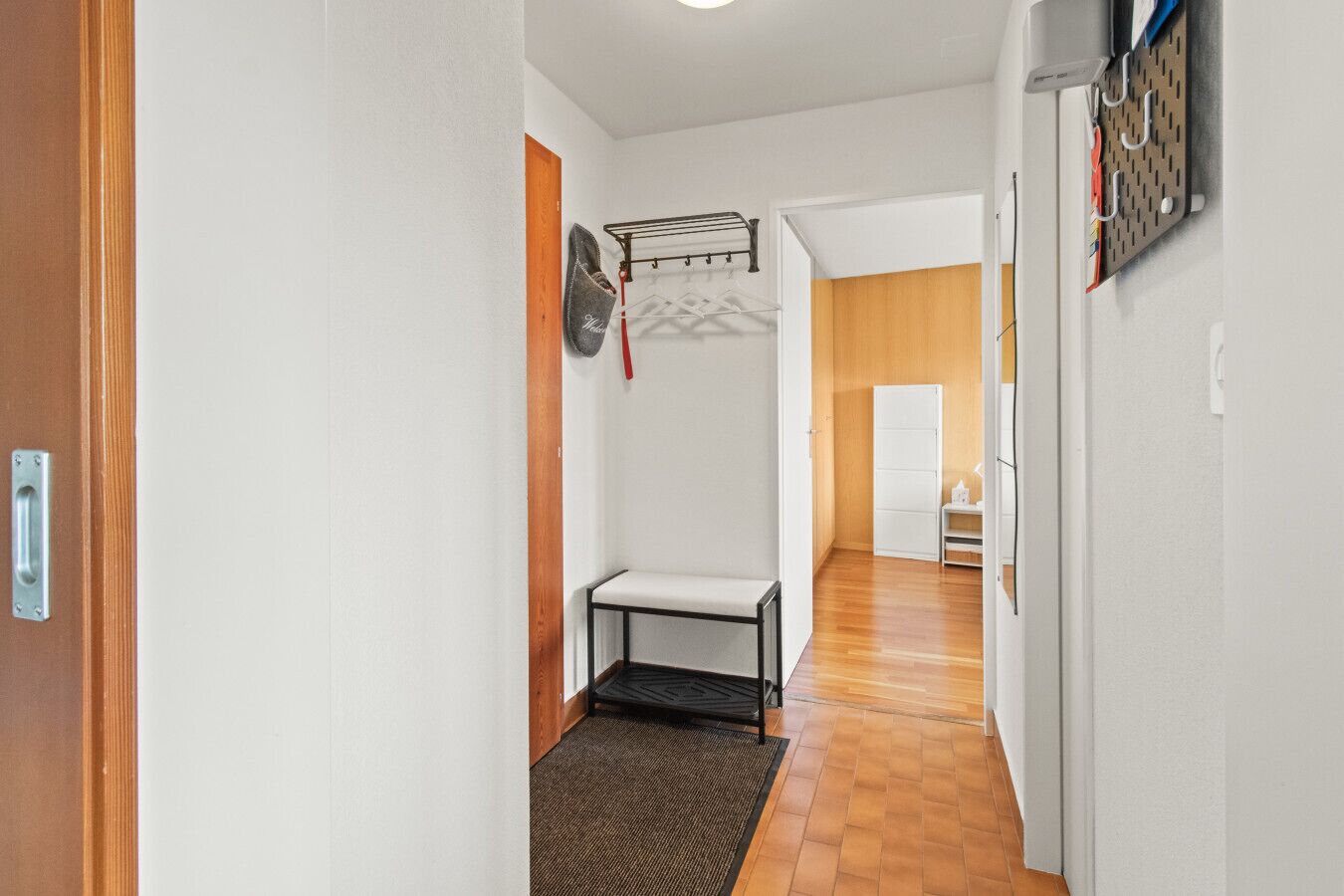 Un pasillo con un banco, un tendedero y una puerta que da a otra habitación.