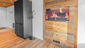 A modern interior with a wooden wall panel, a black cabinet, and a fireplace with a fire display. - Studio type chalet plein centre (Crans-Montana)