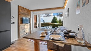 A modern kitchen with a dining area, wooden accents, and a view of the outside. - Studio type chalet plein centre (Crans-Montana)
