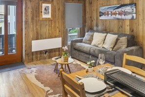 Un salon confortable avec un canapé, une table à manger dressée pour deux personnes et un téléviseur fixé au mur.