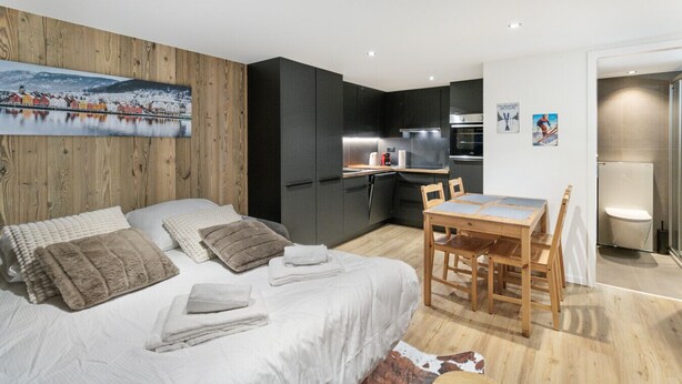 A modern bedroom with a bed, bedside tables, a wooden headboard, a small kitchenette, and a bathroom.