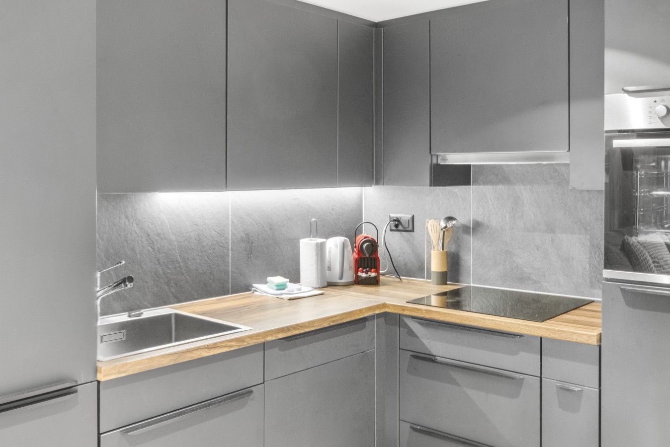Una cocina moderna con armarios grises, encimera de madera, pileta de acero inoxidable y horno empotrado.