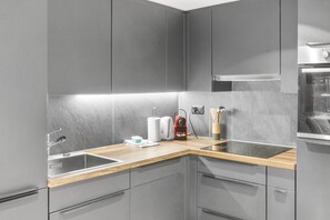 A modern kitchen with grey cabinetry, a wooden countertop, a stainless steel sink, and a built-in oven. - Elegant studio in the heart of the Alps (Saas-Fee)