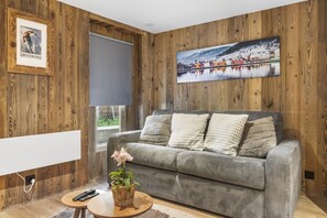 A living room with a grey sofa, a large painting, and a wooden wall. - Elegant studio in the heart of the Alps (Saas-Fee)