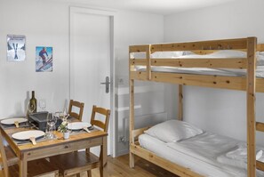 A bunk bed room with a wooden table and chairs, a door, and two framed pictures on the wall. - Elegant studio in the heart of the Alps (Saas-Fee)