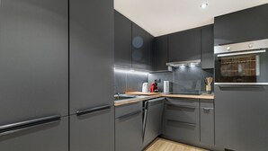 A modern kitchen with dark cabinetry, a wooden countertop, a built-in oven, and a stainless steel range hood.