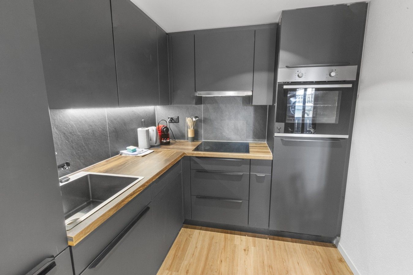 A modern kitchen with dark cabinetry, a wooden countertop, and a built-in oven.