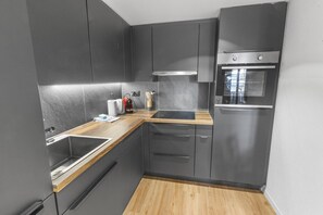 A modern kitchen with dark cabinetry, a wooden countertop, and a built-in oven. - Elegant studio in the heart of the Alps (Saas-Fee)