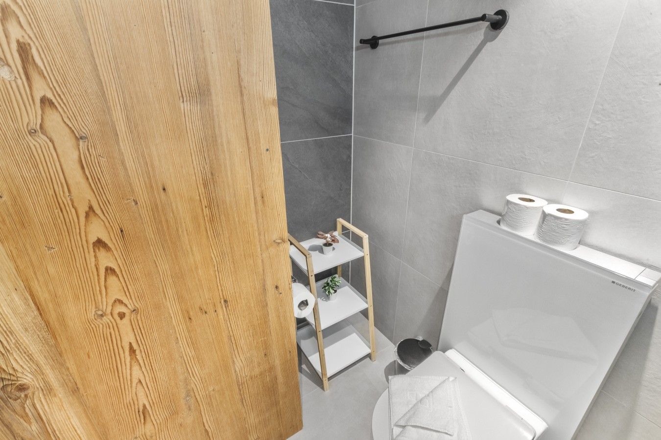 Ein Badezimmer mit Holztür, Toilette in Weiß, Ablagefläche für Toilettenartikel und Handtuchhalter.
