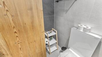 Ein Badezimmer mit Holztür, Toilette in Weiß, Ablagefläche für Toilettenartikel und Handtuchhalter.