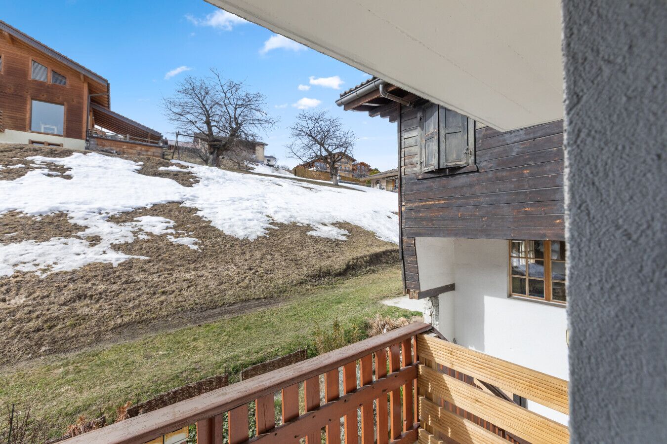 Un balcon en bois offrant une vue sur une colline enneigée et des bâtiments en arrière-plan.