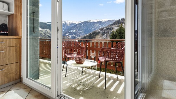 A balcony with a table and chairs, a glass door, and a view of snow-capped mountains.