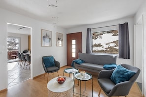 A modern living room with a grey sofa, two armchairs, a coffee table, and a dining area with a table and chairs.