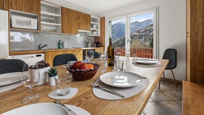 A modern kitchen with wooden cabinets, a dining table set for four, and a view of mountains through large windows.