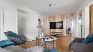 A modern living room with a flat-screen TV, two grey armchairs, a small coffee table, and a striped wall.