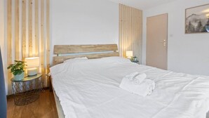 A neatly made bed with white linens and towels, a wooden headboard, a bedside lamp, and a small potted plant on a bedside table.