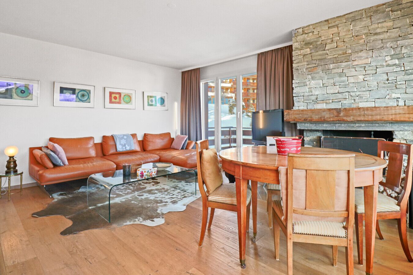 Ein modernes Wohnzimmer mit einer Ledersofa, einem Glastisch und einem Holzespeisesaal mit Stühlen. Ein Kamin aus Stein und ein großes Fenster mit Vorhängen sind ebenfalls vorhanden.