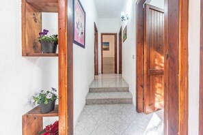 A hallway with wooden doors, a tiled floor, and a wooden shelf with potted plants.
