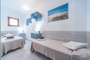 A hotel room with two beds, a window, a painting of a beach, and a small desk with a lamp.
