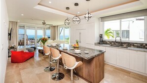 A modern kitchen with a central island, bar stools, and a view of the ocean. - La Vista #B06, gorgeous Ocean View Condo (Playa Tamarindo, Guanacaste Province)