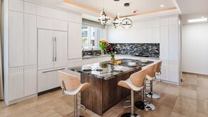 A modern kitchen with white cabinetry, a central island with bar stools, and a black backsplash. - La Vista #B06, gorgeous Ocean View Condo (Playa Tamarindo, Guanacaste Province)