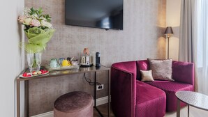 A modern living room with a flat-screen TV, a pink sofa, a small round table, and a coffee station. - Deluxe With St. Mark's Square View (Venezia)