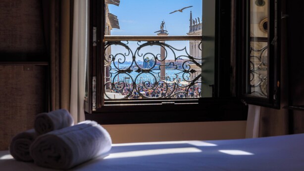 A window with a view of a busy harbor and a statue, with two rolled towels on the windowsill. - Deluxe With St. Mark's Square View (Venezia)