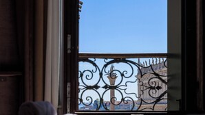 A hotel room with a bed, rolled towels, and a view of a balcony with a wrought iron railing. - Deluxe With St. Mark's Square View (Venezia)