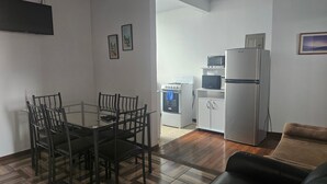 A compact living space with a dining table and chairs, a kitchenette with a microwave and refrigerator, and a sofa.
