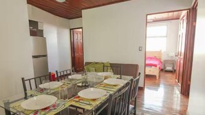A dining area with a glass table set for four, a wooden ceiling, and a view into a bedroom.