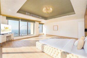 A spacious bedroom with a large bed, a desk, and a view of a Ferris wheel through large windows.